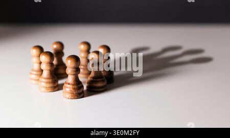 Ein fesselndes Foto von hölzernen Schachspielern, die dicht auf einer weißen Oberfläche stehen und dramatische lange Schatten werfen. Stockfoto