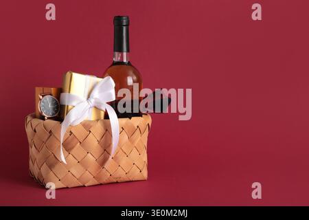 Geschenkkorb mit männlichen Accessoires, Flasche Wein und Geschenk auf rotem Hintergrund Stockfoto