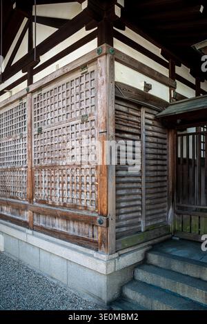 Detaillierte Ansicht einer verwitterten hölzernen Tempelecke mit Gitterplatten in Imamiya Ebisu Jinja, horizontalen Latten und Steintreppen, die Tradition zeigen Stockfoto