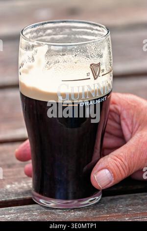 Hand mit einem Pint Guinness Bier vom Fass mit cremigem Kopf auf einem Holztisch Stockfoto