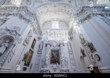 Ein detaillierter Blick auf einen kunstvoll verzierten Seitenaltar mit weißen barocken Stuckskulpturen und religiösen Gemälden in der Kirche St. Peter und St. Paul in Vilnius. Stockfoto