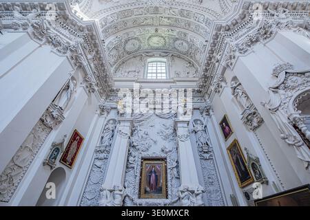 Ein detaillierter Blick auf einen kunstvoll verzierten Seitenaltar mit weißen barocken Stuckskulpturen und religiösen Gemälden in der Kirche St. Peter und St. Paul in Vilnius. Stockfoto