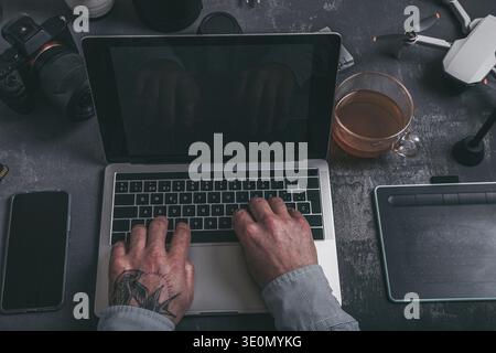 Professionelle Hände, die auf der Laptop-Tastatur tippen, umgeben von kreativen technischen Tools Stockfoto