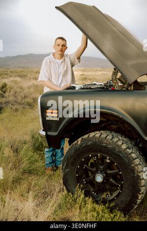 Ernsthafter junger Mann, der den Motor in landschaftlich reizvoller Natur überprüft Stockfoto
