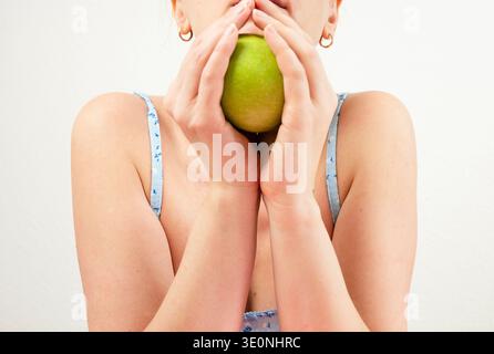 Eine junge Frau, die grünen Apfel vor dem Gesicht hält Stockfoto
