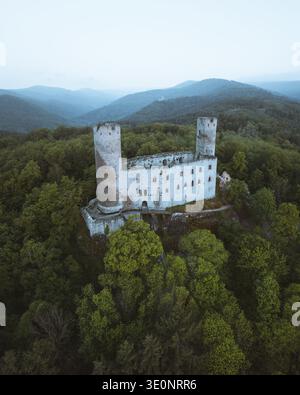 Aus der Vogelperspektive auf eine mittelalterliche Burgruine, die aus einem Meer aus smaragdgrünen Baumkronen vor dem Hintergrund der trüben blauen Berge ragt, Andlau, Grand Est, Frankreich Stockfoto