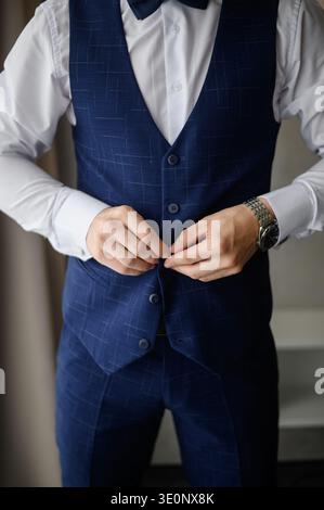 Nahaufnahme: Hände knöpfen dunkelblaue Weste. Der Bräutigam passt seine elegante Weste an. Morgenritual und klassische Hochzeits-Raffinesse. Herrenstyle-Konzept, Busi Stockfoto