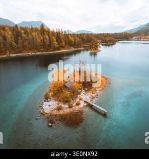 Blick aus der Vogelperspektive auf die bezaubernde Insel mit einem winzigen Haus, umgeben von türkisfarbenem Seenwasser und lebhaftem Herbstlaub, Grainau, Bayern, Deutschland. Stockfoto