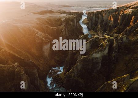 Aus der Vogelperspektive auf den Serpentinfluss, der durch die zerklüfteten, moosbedeckten Klippen des Fjadrargljufur Canyon schneidet und eine dramatische Landschaft unter dem schafft Stockfoto