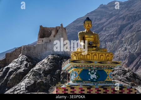 Eine goldene Buddha-Statue sitzt auf einem reich verzierten Sockel vor den alten, ruinierten Steinmauern der Festung in Charasa. Stockfoto