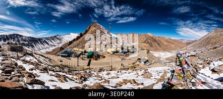 Dieser weite Panoramablick zeigt die Infrastruktur und Gebetsflaggen in Khardung La vor einem riesigen Berghorizont. Stockfoto