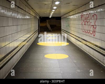 Schwach beleuchtete Fußgängerunterführung, beleuchtet durch Deckenleuchten mit gelben runden Bodenmarkierungen und Graffiti an den Wänden in Coventry uk Stockfoto