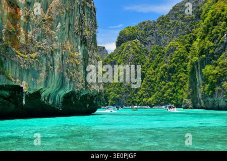 Langboot-Boote und Touristen, die das türkisfarbene Wasser der Maya Bay auf Ko Phi Phi Leh in der Provinz Krabi, Thailand, betreten, umgeben von dramatischem Kalkstein Stockfoto