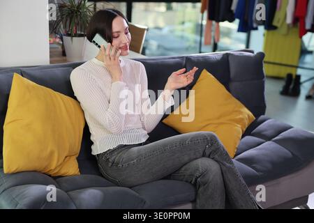 Die junge Frau genießt einen trendigen Moment, während sie sich auf einem gemütlichen Sofa in einem lebendigen modernen Raum entspannt Stockfoto