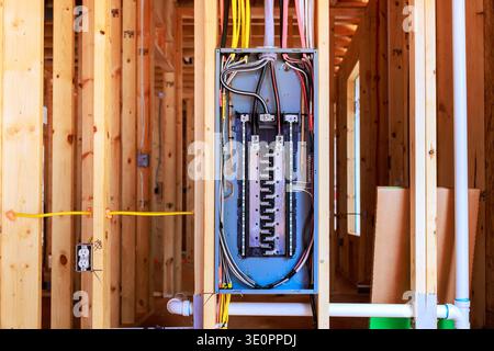 Arbeiter installieren eine elektrische Schalttafel in einem neu erbauten Haus mit Holzrahmendrähten in Sichtweite. Stockfoto