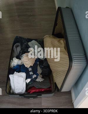 Offener Reisekoffer, gefüllt mit Kleidung, während der Verpackung zu Hause. Stockfoto