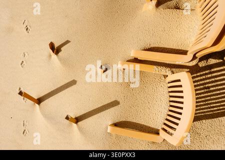Eine minimalistische Küstenszene am Faro Beach, Algarve, Portugal, mit Plastikstühlen, die nach Winterstürmen teilweise in Sand vergraben sind. Einige Stühle bleiben u Stockfoto