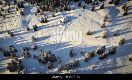 Aus der Vogelperspektive einer einsamen Hütte, eingebettet in eine unberührte, schneebedeckte Landschaft, mit langen Schatten, die sich über das hügelige Gelände erstrecken, Gingins, Stockfoto