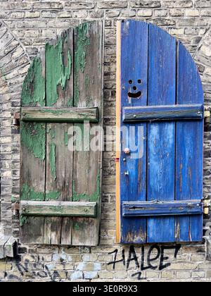 Ein Paar grüne und blaue Rollläden sind mit abblätternder Farbe gegen eine Ziegelwand im Freetown Christiania Viertel von Kopenhagen verwittert. Stockfoto