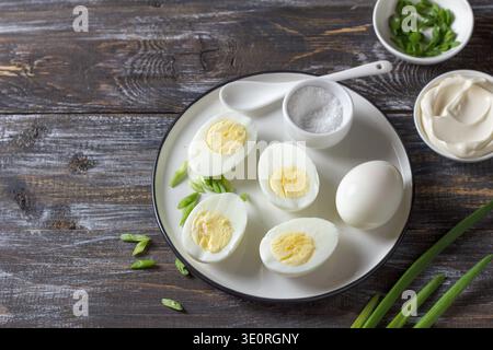 Gekochte Eier mit grüner Zwiebel, Salz und Mayonnaise auf Teller auf Holztisch Stockfoto