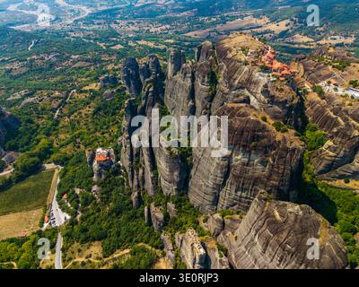 Blick aus der Vogelperspektive auf dramatische Felsformationen mit Klöstern, die sich in die üppige grüne Landschaft von Meteora, Trikala, Griechenland, einfügen. Stockfoto