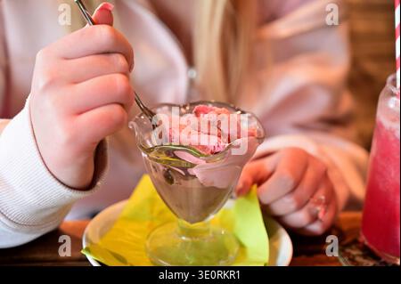 Nahaufnahme einer Person, die einen köstlichen Eisbecher aus Erdbeeren und Schokolade mit einem Löffel genießt Stockfoto