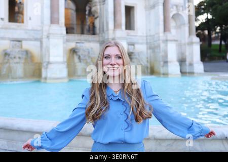 Glückliche junge Frau, die in der Nähe des historischen Marmorbrunnens in Rom lächelt. Porträt mit schöner europäischer Architektur. Stockfoto