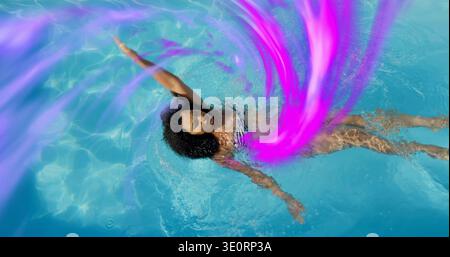 Schwimmende Frau mit gestreiftem Bikinioberteil, die hinten im Außenpool herumdriftet, magentafarbene Bänder Stockfoto