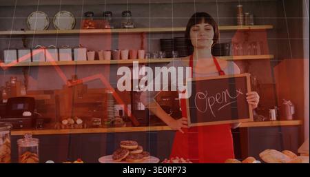 Frau in roter Schürze, die ein Schild mit der Aufschrift Open hinter der Backstube mit Donuts und Kaffee hält Stockfoto