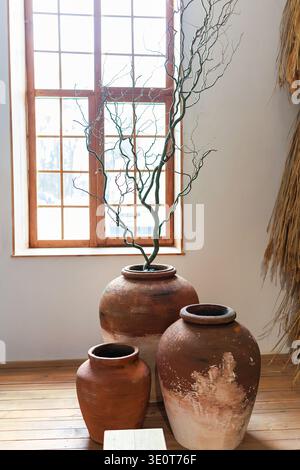 Rustikale handgefertigte große Tonkeramikvasen und trockene Zweige. Boho- oder Wabi-Sabi-Innenausstattung mit natürlichen Materialien. Terrakotta-Keramikgläser Stockfoto