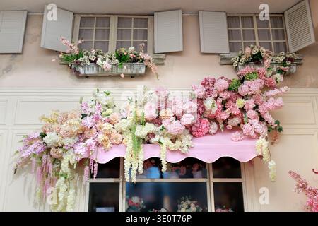 Wunderschöne Blumendekoration an einer alten Gebäudefassade mit Blumen und blühenden Gestaltungselementen um ein Fenster. Stockfoto