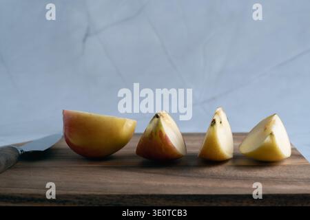 Mehrere frische rote und gelbe Apfelkeile ordentlich auf einem rustikalen Holzschneidebrett neben einem Küchenmesser angeordnet Stockfoto