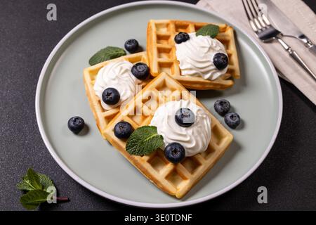 Frisch gebackene Waffeln mit süßer Schlagsahne, frischen Heidelbeeren und duftenden Minzblättern sorgen für ein köstliches und einladendes Desse zum Frühstück Stockfoto