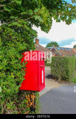 Eversley, Großbritannien - 21. September 2025: Ein traditioneller roter britischer Postkasten, eingebettet in eine üppig grüne Hecke. Stockfoto
