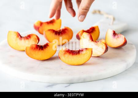 Geschnittene Segmente von freien Steinpfirsichen auf einer Marmorplatte mit einer Hand nach innen. Stockfoto