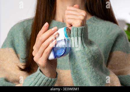Frau mit Stoffrasierer auf Wollpullover und entfernt Fussel und Fuzz. Konzept der Langlebigkeit der Garderobe verlängert die Lebensdauer der Kleidung und behält die Strickqualität bei. Stockfoto