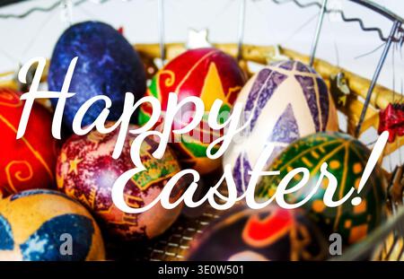 Happy Easter Grußkarte Konzept. Nahaufnahme von traditionell bemalten Ostereiern Pysanky in einem Korb mit elegantem weißem Happy Easter Text Overla Stockfoto