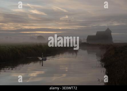 St. Thomas Becket (Fairfield) Kirche auf einem nebeligen Romney Marsh in Kent bei Sonnenaufgang mit Reflexionen im glatten Wasser des Puddledock Kanals Stockfoto