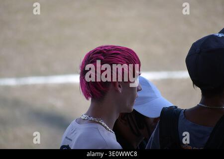 Im Baseballstadion in Ciego de Ávila, Kuba, steht ein junger Fan mit leuchtend rosa Haaren und einer silbernen Kette unter den Zuschauern. Erfasst in Profil agai Stockfoto