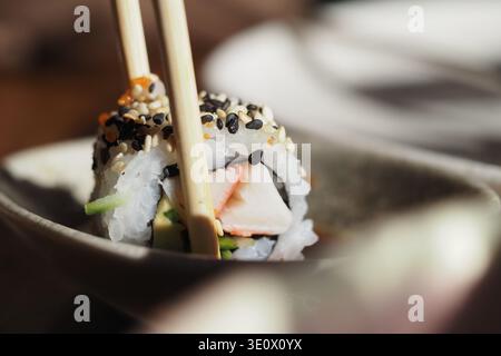 Sushi-Zubereitung auf einem Teller mit Stäbchen, die oben gehalten werden Stockfoto