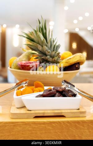 Getrocknete Aprikosen und Datteln in weißen Schüsseln am Frühstücksbuffet mit verschwommenem Obst im Hintergrund Stockfoto