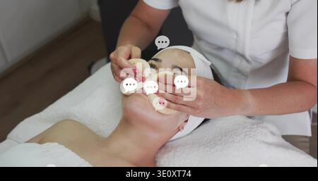Auftragen des Kosmetikers in weißer Uniform, das Wattepads auf den Klienten im Spa drückt, rosa Nagelüberlagerungen Stockfoto