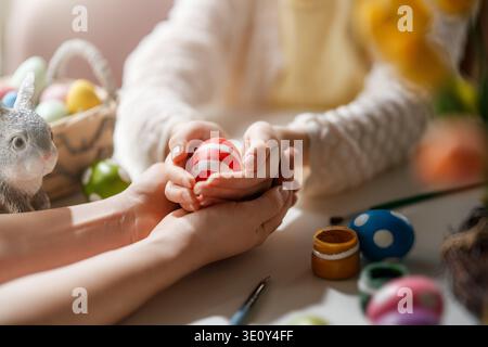 Herzerwärmendes Nahbild, das die emotionale Verbindung zwischen Eltern und Kind feststellt, während sie Ostereier zusammen schmücken. Sanftes Sonnenlicht taucht Stockfoto