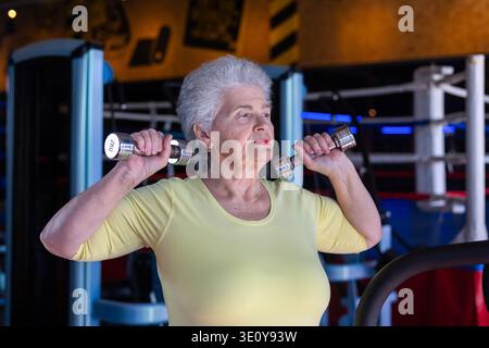 Grauhaarige ältere Frau, die während eines Workouts Kurzhanteln hebt und durch regelmäßiges Wiegen Fitness, Vitalität und Muskelerhaltung der Senioren demonstriert Stockfoto