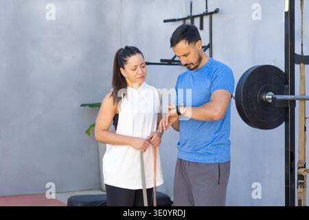 Personal Trainer überprüft die Zeit auf seiner Smartwatch, während er mit einer Kundin während eines Workouts im Freien arbeitet, und demonstriert die Verwendung von Technol Stockfoto