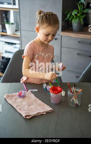 Fokussiertes Kind fügt farbigen Ostereiern mit feinem Pinsel Details hinzu. Steht für künstlerische Geduld und saisonale Feierlichkeiten. Stockfoto