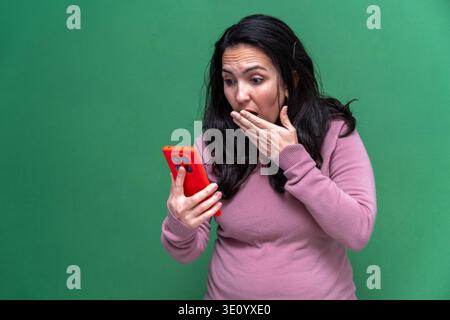 Die überraschte Reaktion der jungen Frau, während sie ihr rotes Smartphone ansah und ihren Mund mit der Hand bedeckte Stockfoto