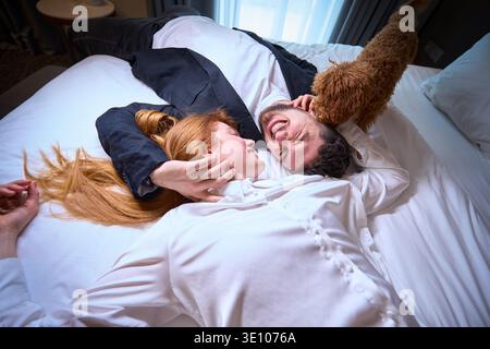 Glückliches junges Paar, das tagsüber im gemütlichen Schlafzimmer mit Hund spielt Stockfoto
