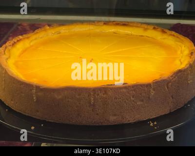 Whole Cheesecake on Bakery Display, Ein wunderschön präsentierter ganzer Käsekuchen, der in einer Bäckerei präsentiert wird und seine cremige Textur und die goldene Kruste hervorhebt Stockfoto