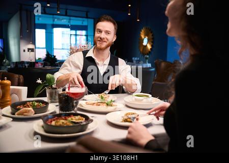 Ein lächelnder Mann, der abends mit einer Frau in einem gemütlichen Restaurant isst Stockfoto